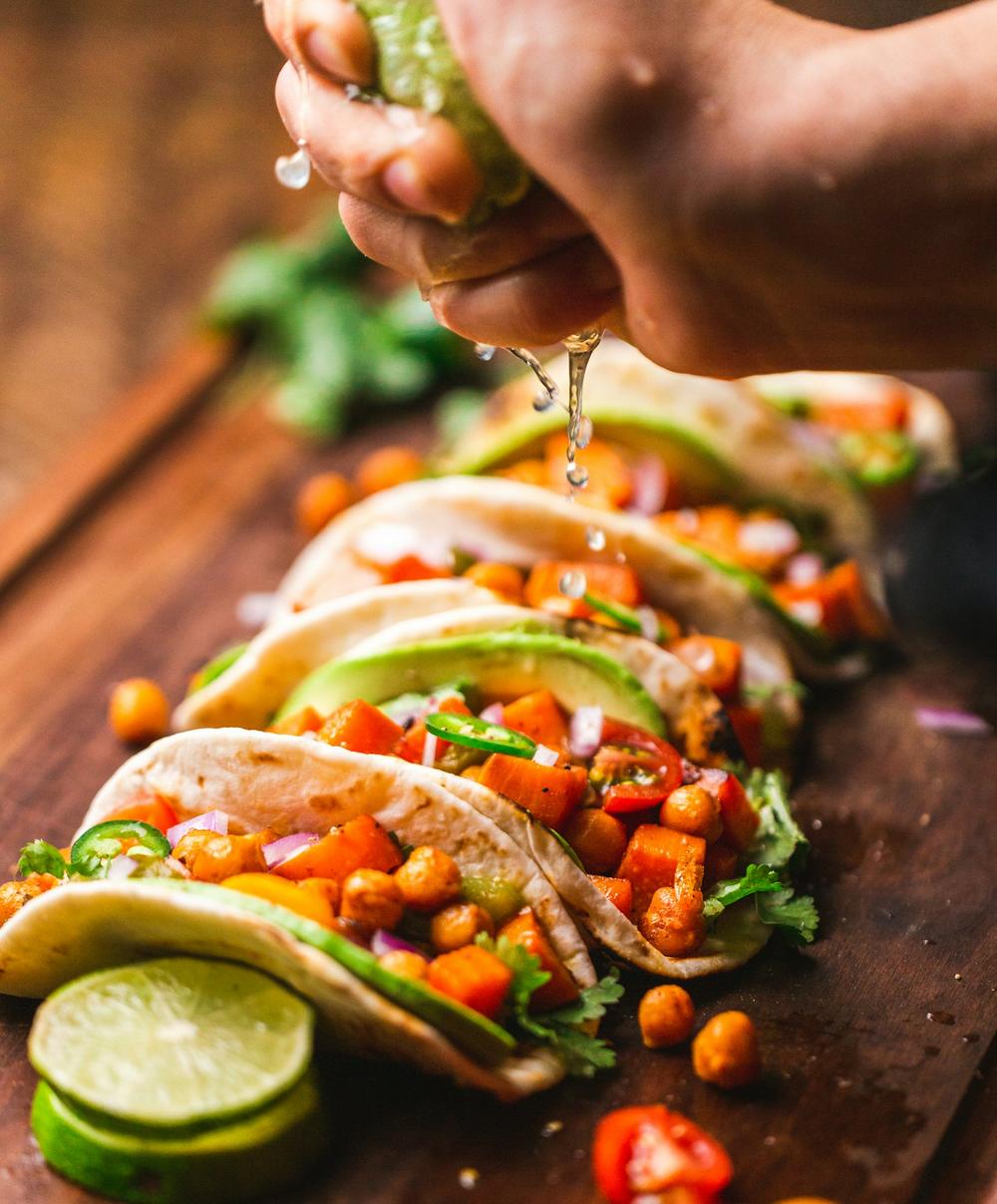 Three tacos with grilled meat, salsa, and lime on a wooden board